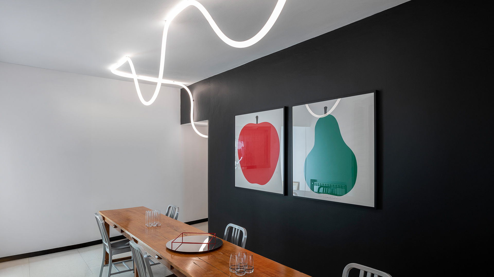Lounge ufficio moderno con lampada a sospensione circolare Artemide La Linea che illumina un'area salotto con sedie blu e rigogliosa vegetazione