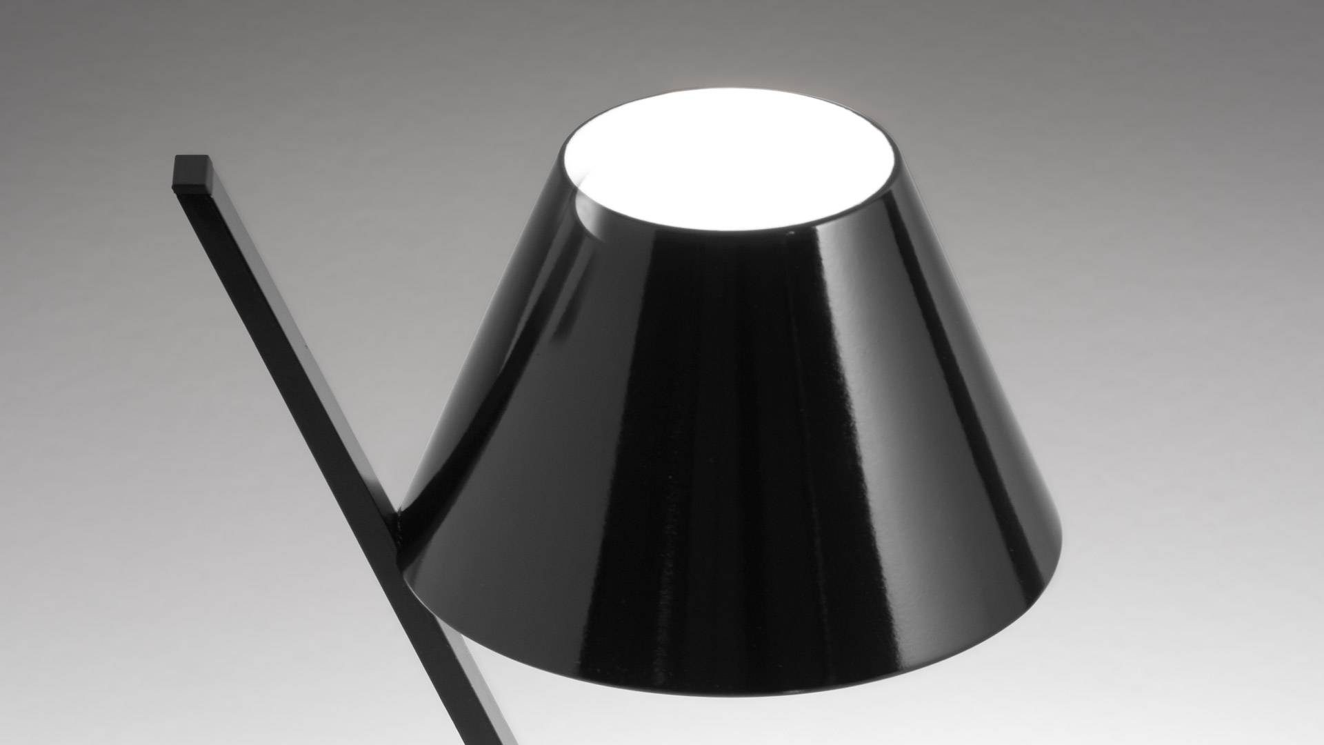 Camera da letto moderna con parete blu-grigia, testiera in legno chiaro, biancheria bianca e una piccola lampada Artemide La Petite Table sul comodino
