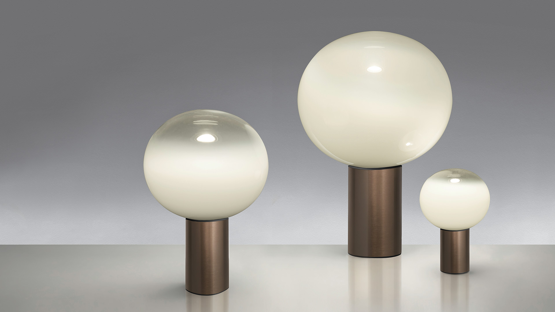 Due lampade da tavolo Artemide Laguna Tavolo con sfere in vetro opalino su basi scure, poste su tavolini bianchi accanto a una poltrona rosa