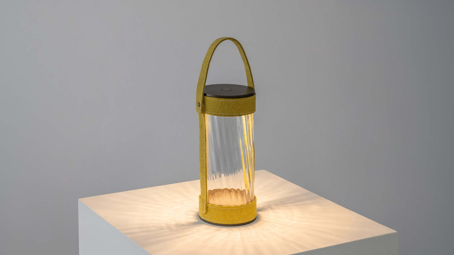 Dettaglio della lampada portatile Artemide Laya: corpo cilindrico scuro con cinghia in tessuto intrecciato color terracotta e rivetto in ottone