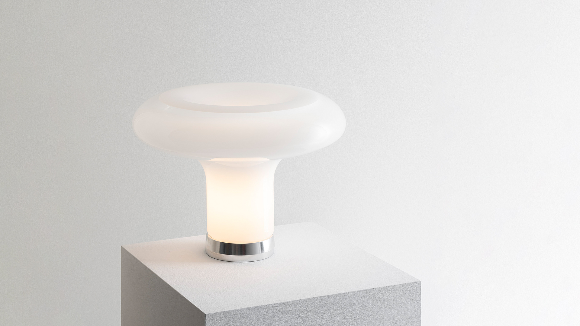 Lampada da tavolo Artemide Lesbo con paralume a fungo in vetro opalino bianco su tavolo di terrazza esterna con balaustra in pietra
