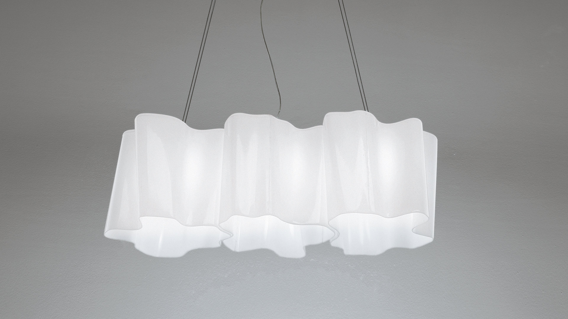 Artemide Logico sospensione 3 in linea: tre diffusori bianchi collegati con morbidi bordi ondulati, appesi a sottili cavi