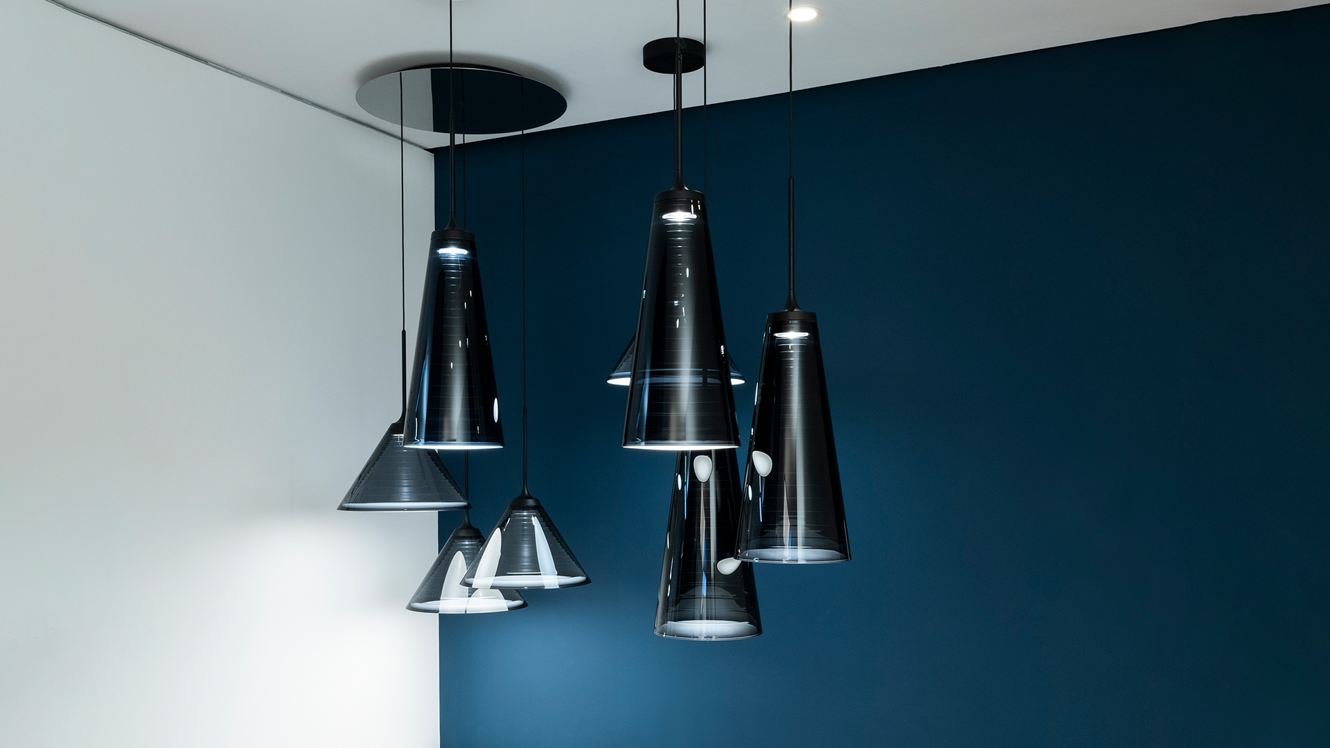 Tre lampade a sospensione coniche nere Artemide 'Look at Me' appese a diverse altezze su sfondo blu profondo