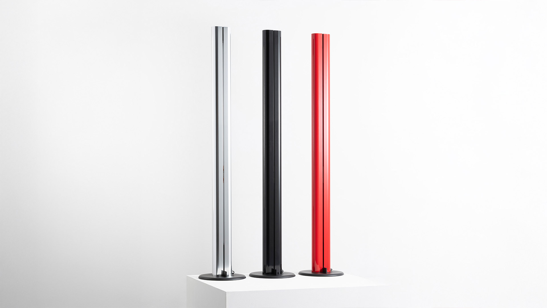 Three Artemide Megaron floor lamps in chrome, black, and red, featuring slim cylindrical columns on round bases