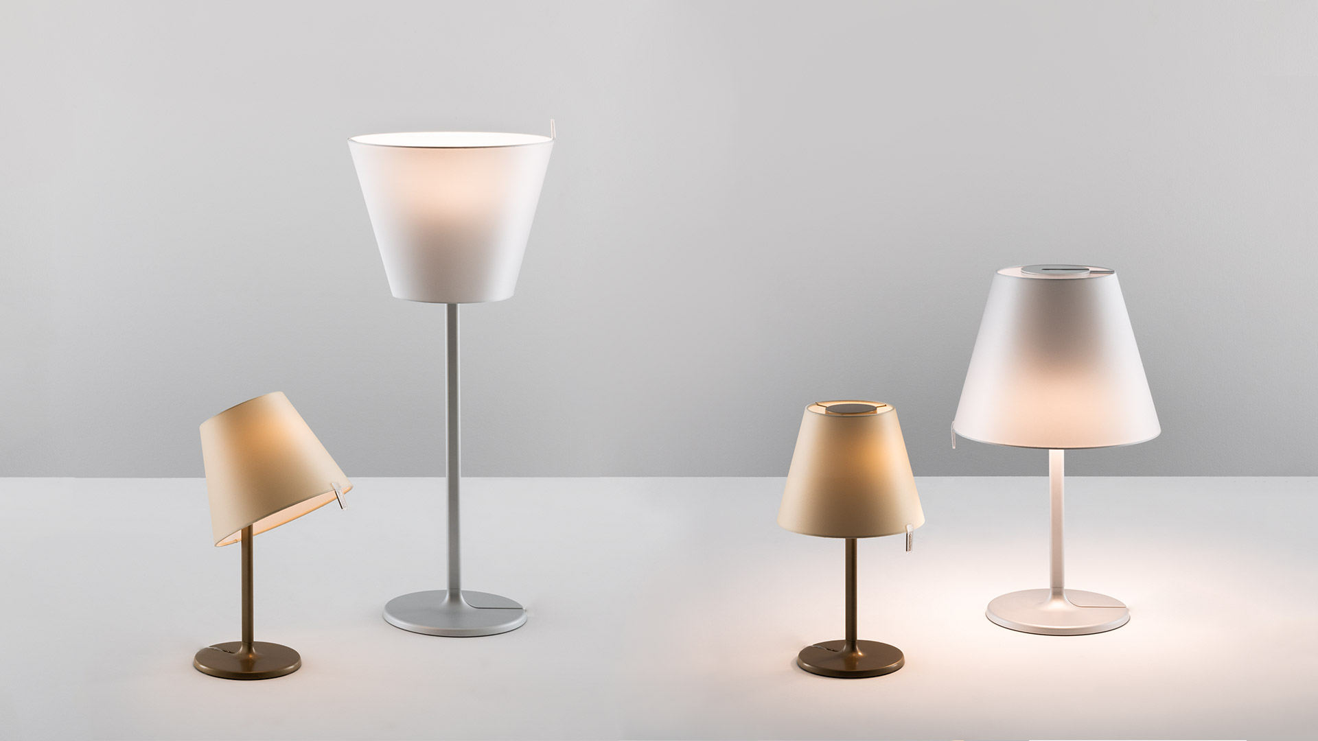 Camera da letto accogliente con letto in legno e biancheria grigia, affiancata da due lampade da tavolo Artemide Melampo Tavolo che emettono luce calda