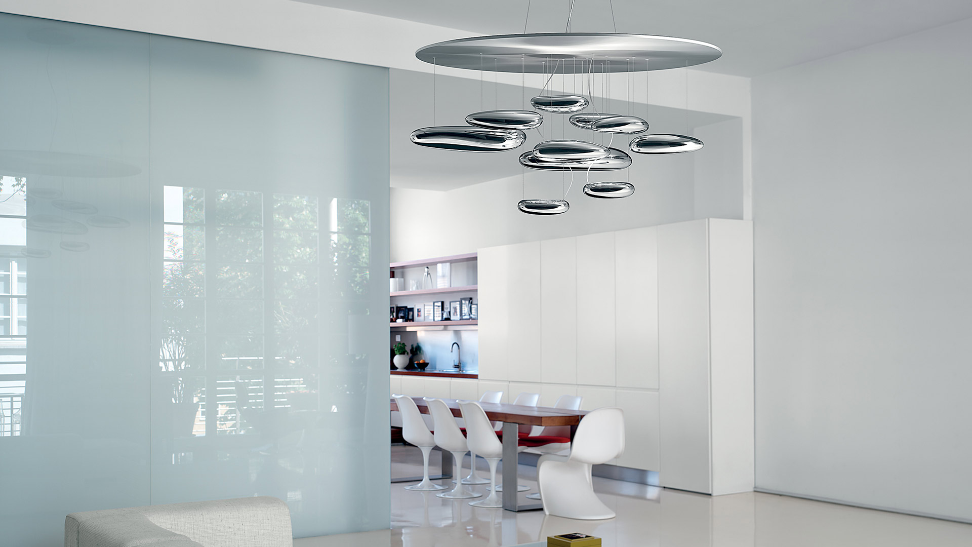 Close-up of Artemide Mercury pendant lamps with polished chrome oval bodies suspended from ceiling, emitting subtle downward light