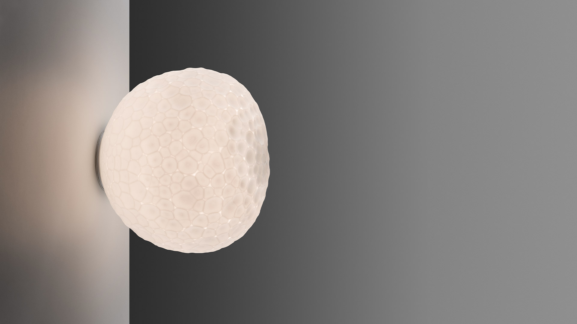 Lampada da parete/soffitto Artemide Meteorite: diffusore sferico bianco con texture a crateri lunari, montata su angolo a parete