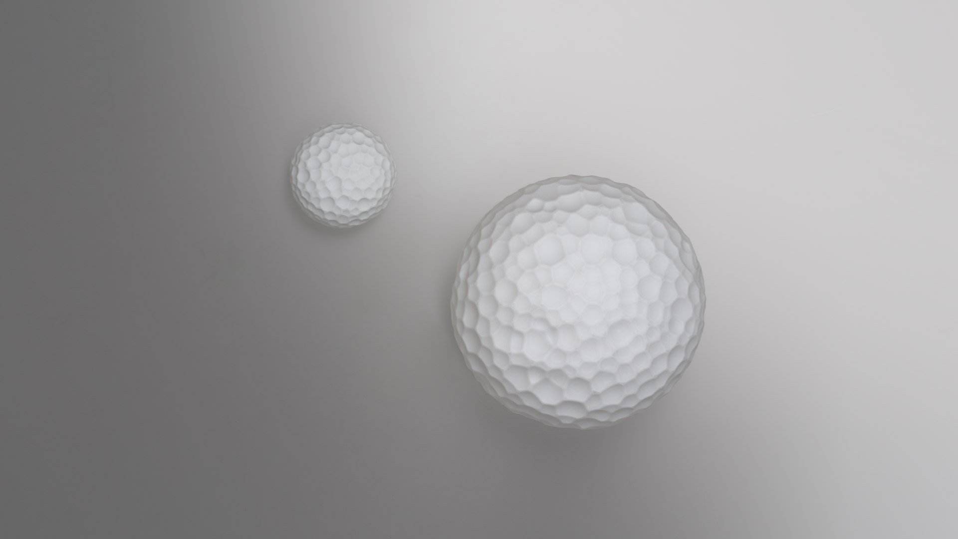Due lampade Artemide Meteorite con diffusori sferici texturizzati: una piccola da parete e una più grande da soffitto su sfondo grigio