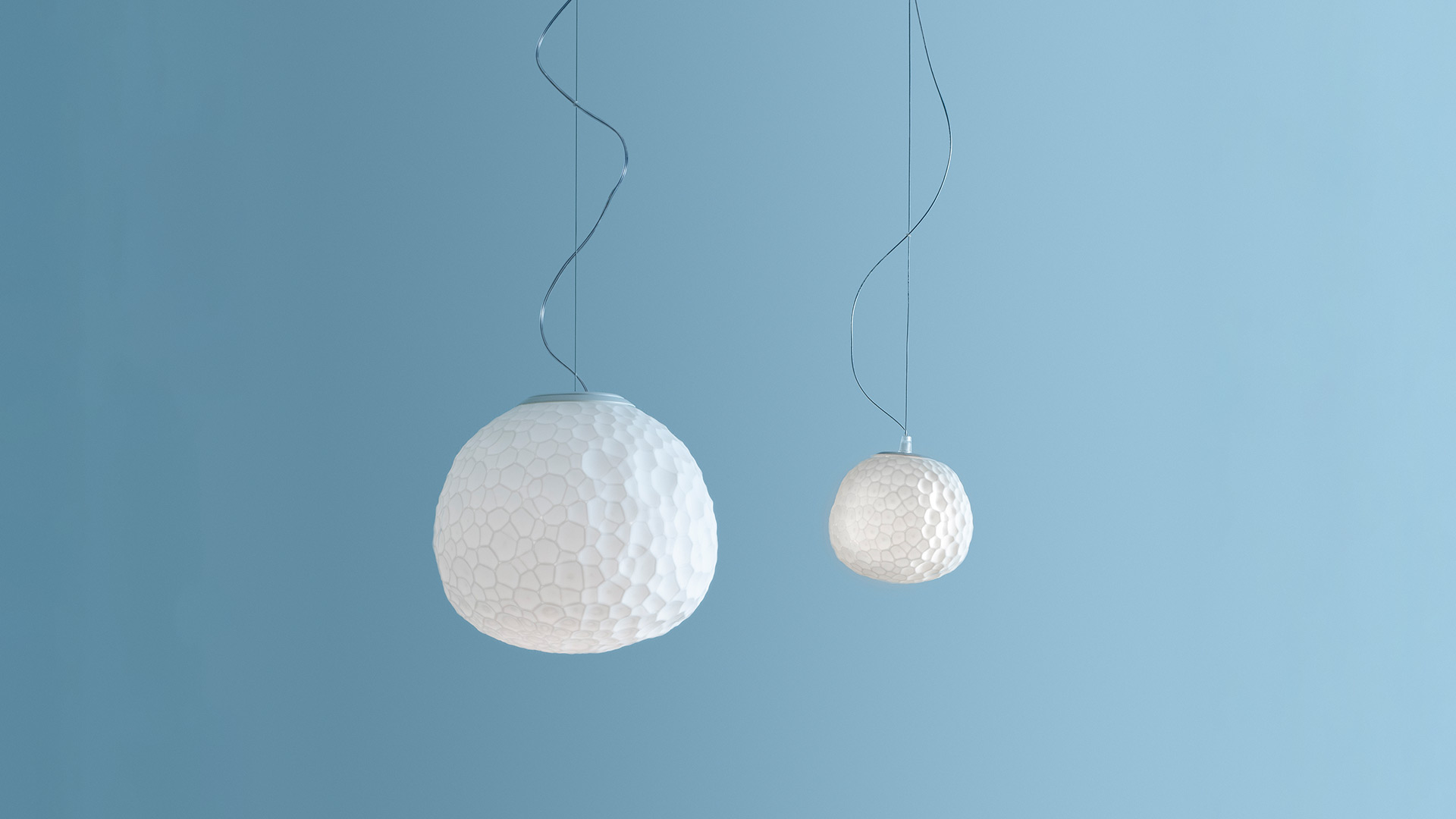 Lampada a sospensione Artemide Meteorite: diffusore sferico bianco opalino con texture cellulare organica, sospeso da un cavo scuro
