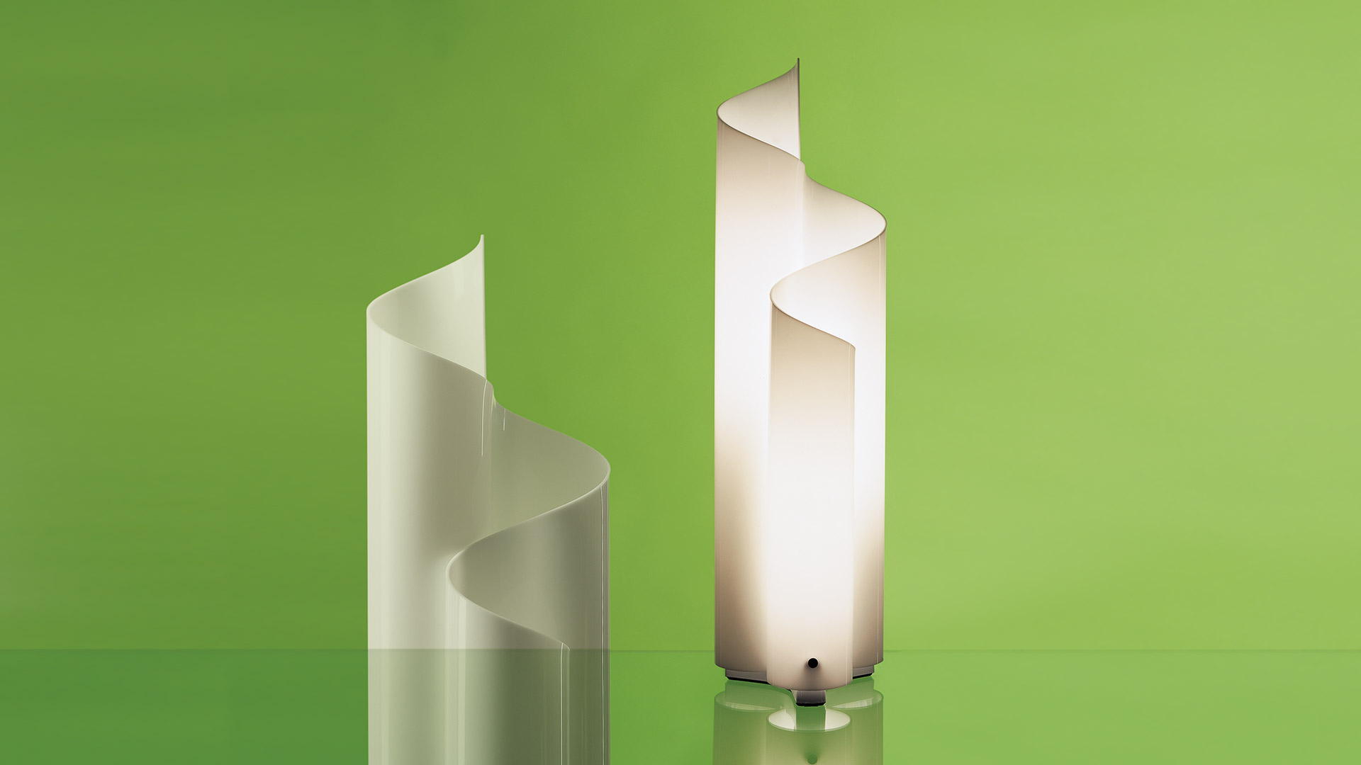 Two Artemide Mezzachimera floor lamps with spiral white polycarbonate shades, one unlit and one illuminated, against a green background