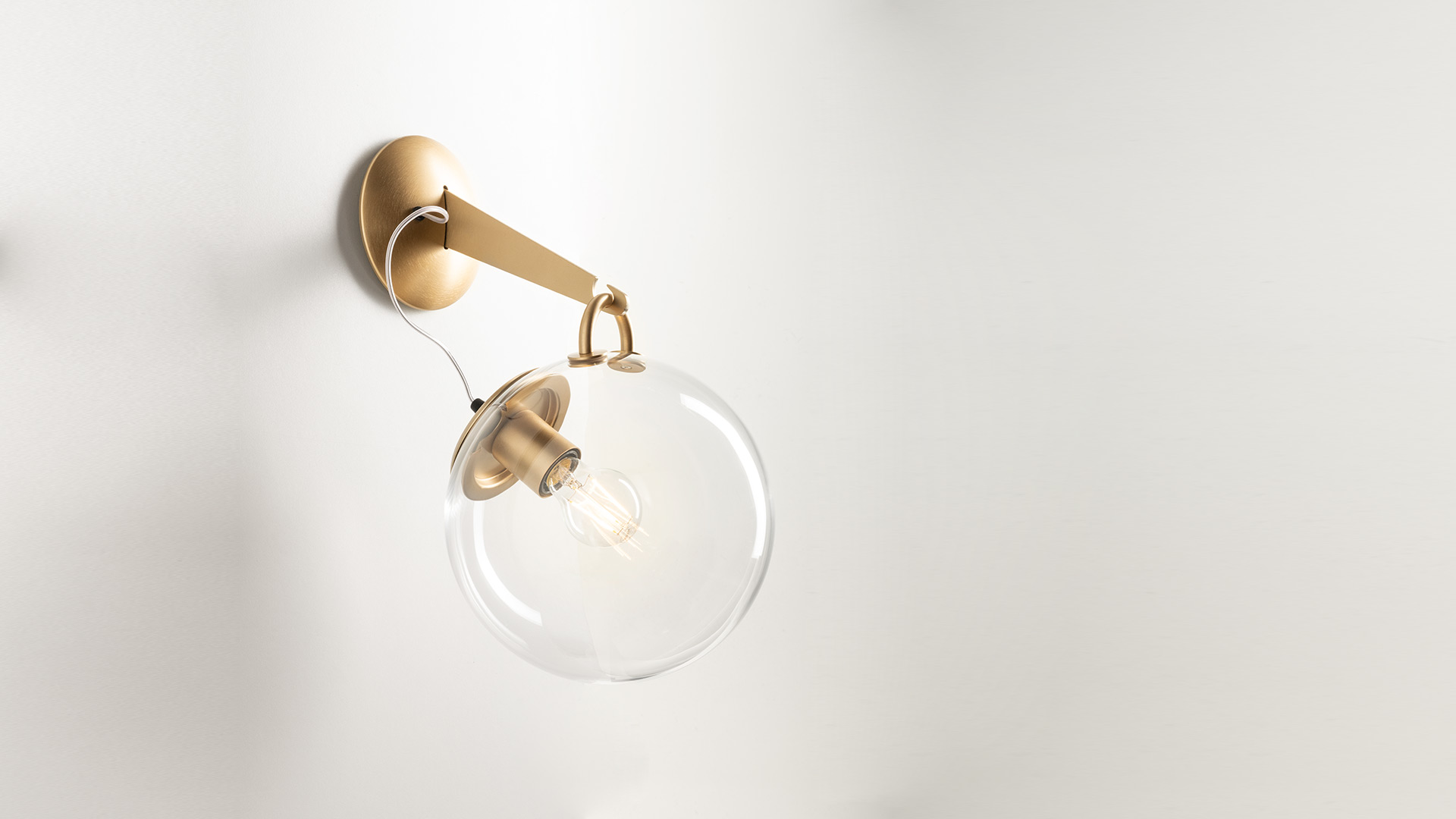 Due lampade a sospensione Artemide Miconos: sfere in vetro trasparente con finiture in ottone, mostrate spenta e accesa, sospese da sottili cavi