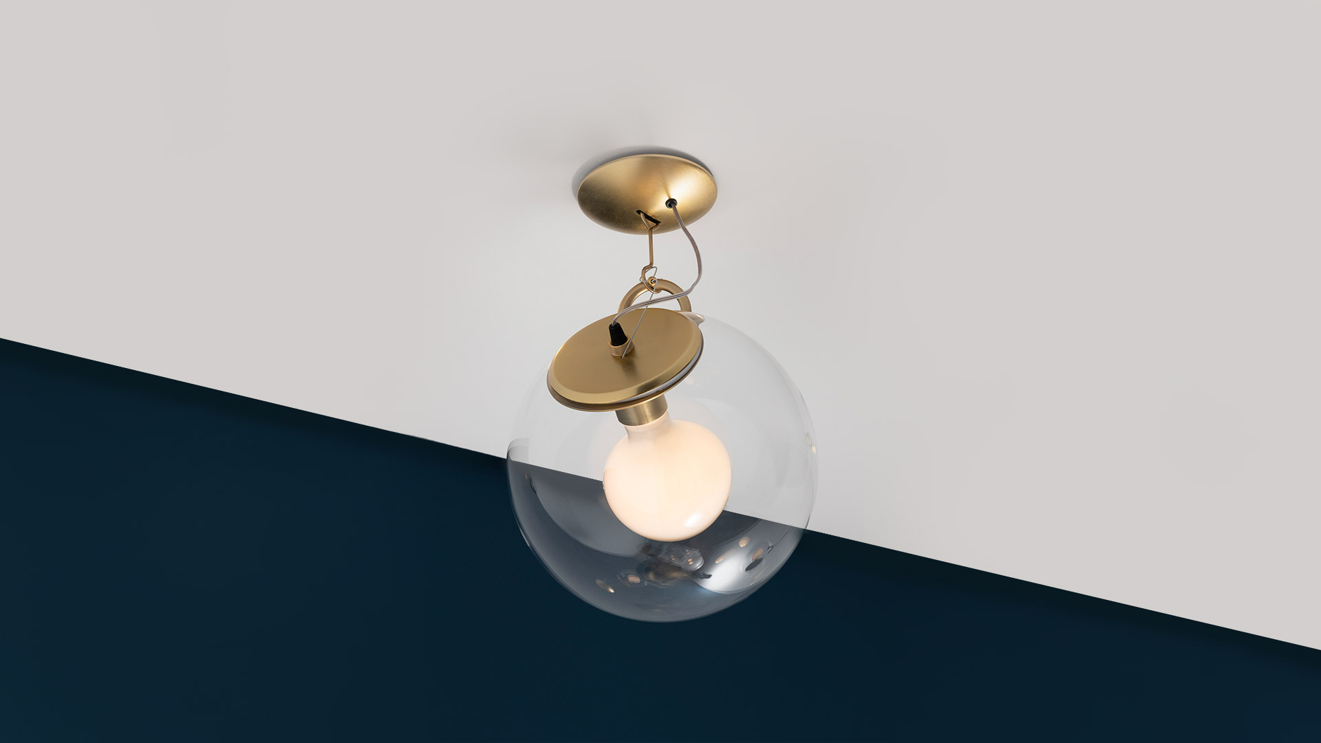 Lampada da parete Artemide Miconos con braccio cromato e diffusore a sfera in vetro trasparente, emette luce calda su parete grigia