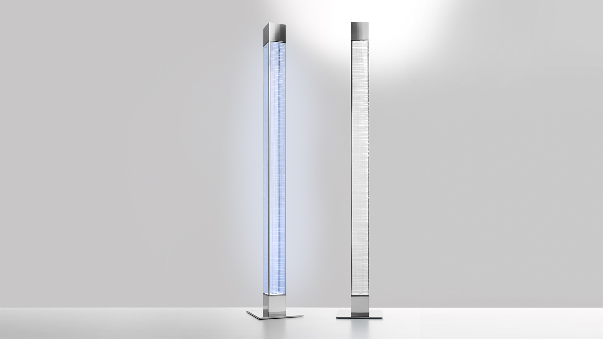 Due lampade da terra Artemide Mimesi: sinistra emette luce blu attraverso colonna in vetro, destra luminosa bianca, entrambe su basi quadrate in metallo