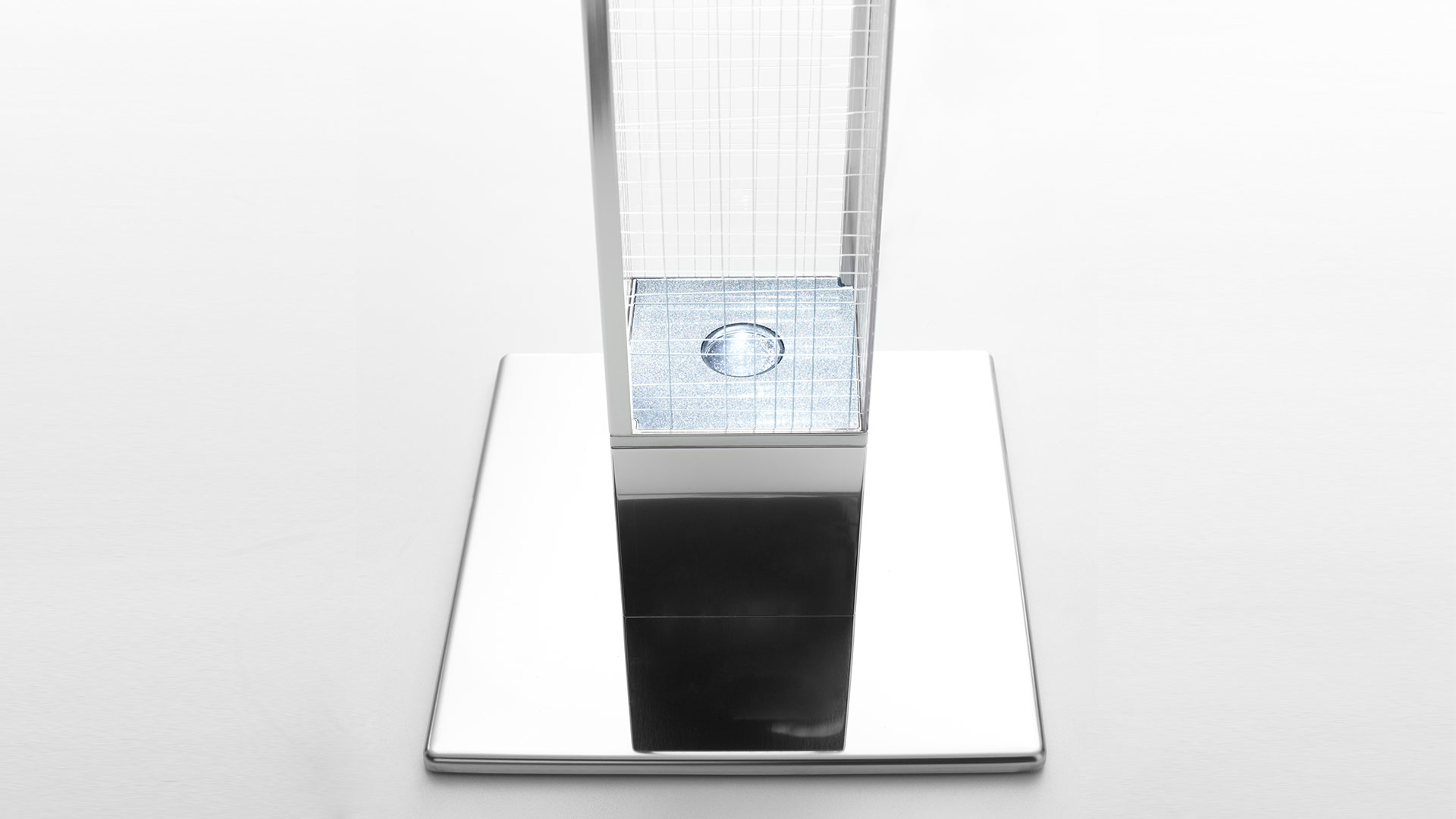 Dettaglio base lampada da terra Mimesi: base quadrata in cromo lucido con sorgente LED visibile attraverso colonna diffusore a griglia trasparente