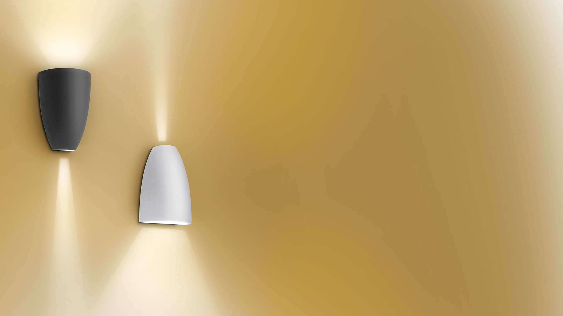 Due applique Artemide Molla su parete dorata: versioni grigio scuro e bianca, con fasci di luce calda verso l'alto e il basso