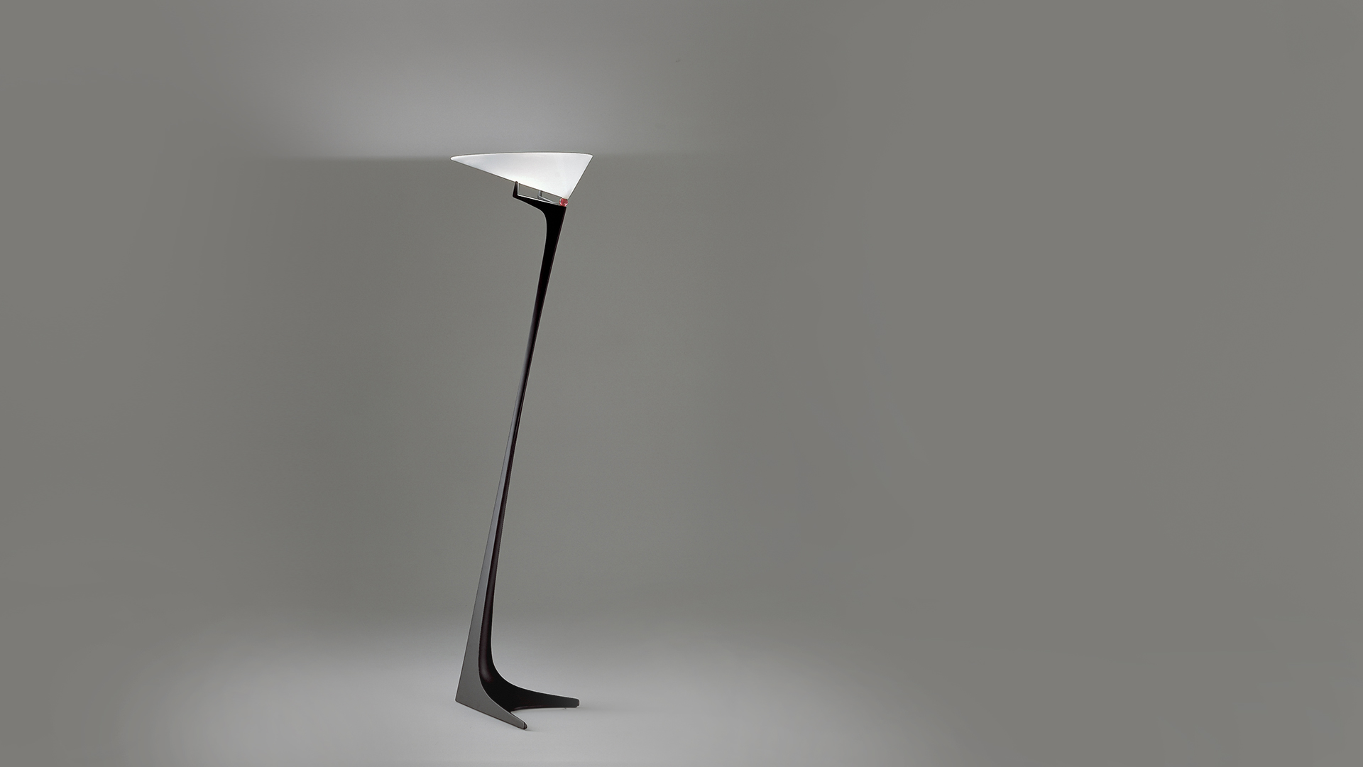 Lampada da terra Artemide Montjuic con base scultorea nera affusolata e diffusore triangolare bianco che emette luce indiretta verso l'alto