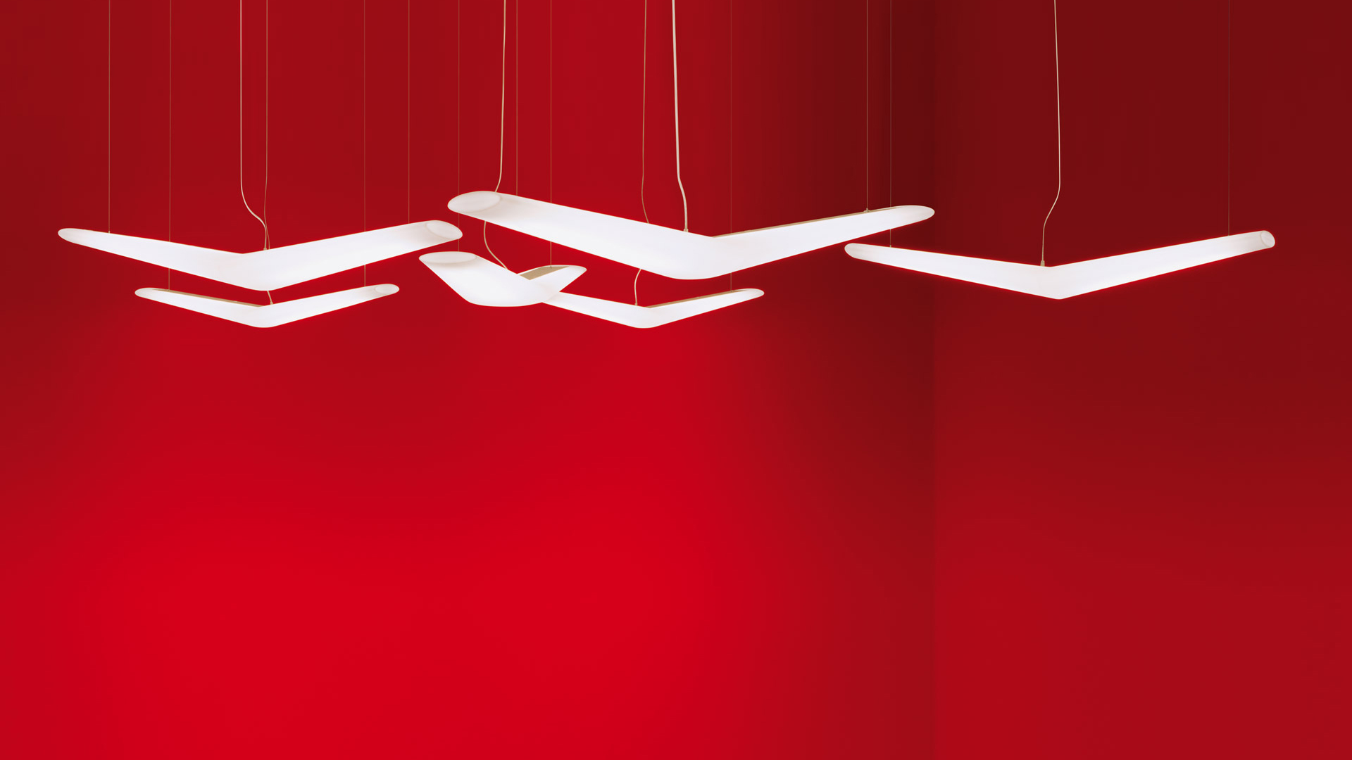 Tre lampade a sospensione Artemide Mouette con diffusori bianchi a forma di ala, sospese da sottili cavi su sfondo rosso