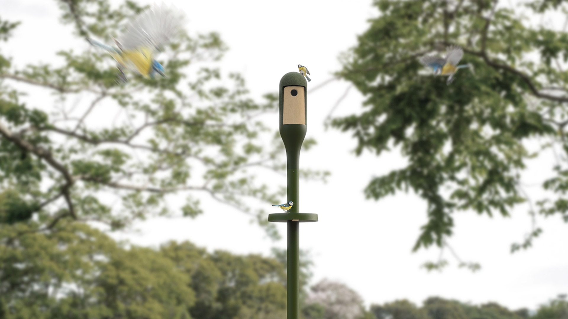 Lampada da esterno Needoo di Artemide: palo verde scuro con testa luminosa a forma di casetta per uccelli, installata in un giardino con alberi