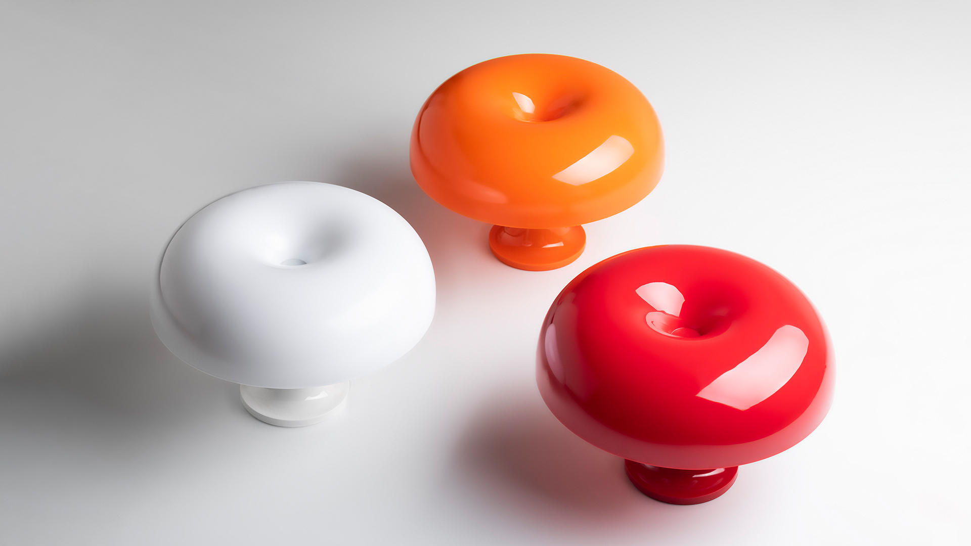 Lampada da tavolo Artemide Nessino in rosso intenso, con iconico paralume a ciambella su base a piedistallo, mostrata con oggetti di design coordinati