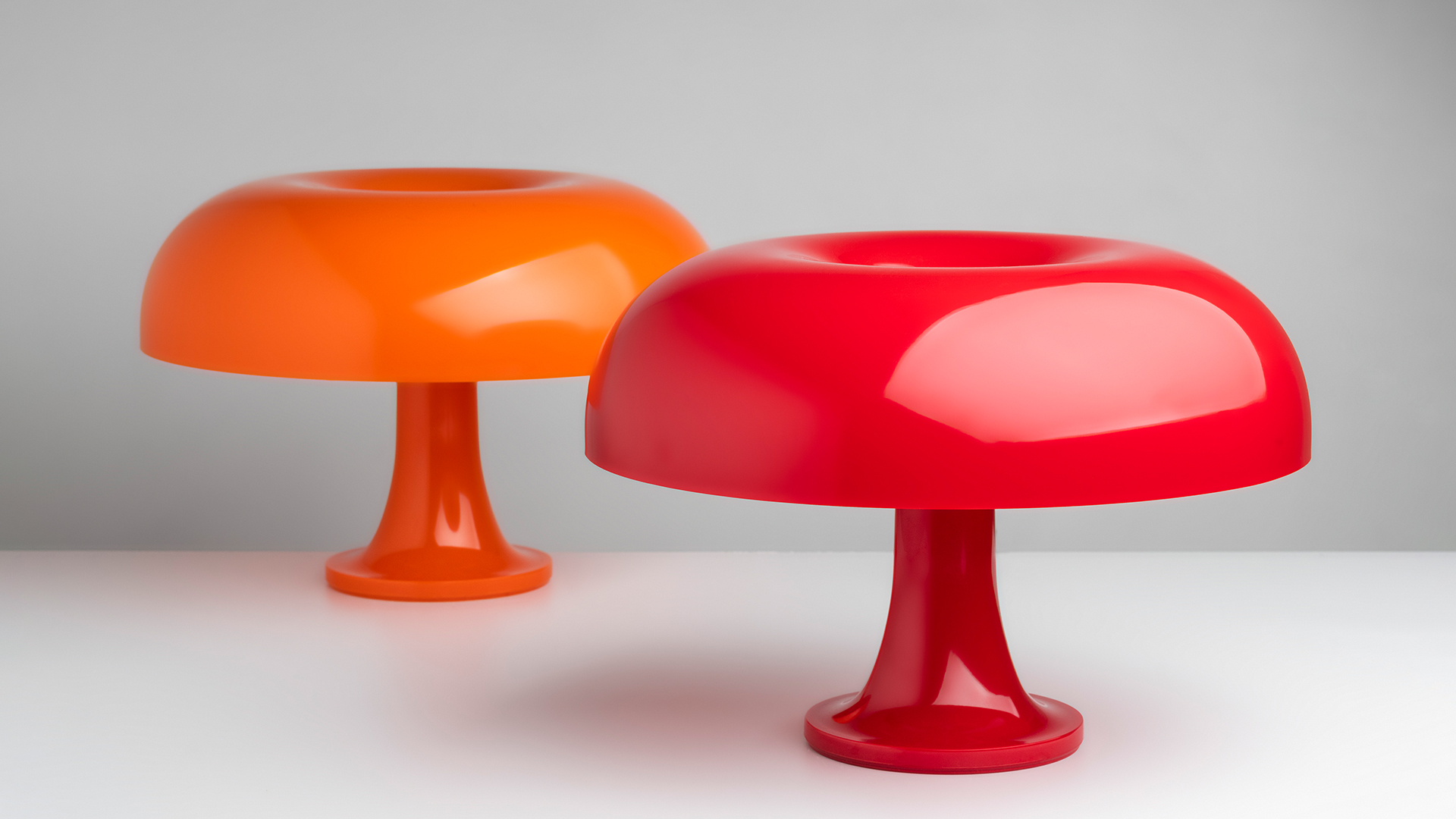 Due lampade da tavolo Artemide Nessino con paralumi a fungo in rosso intenso, esposte su piedistalli cilindrici a gradini davanti a tende di velluto rosso