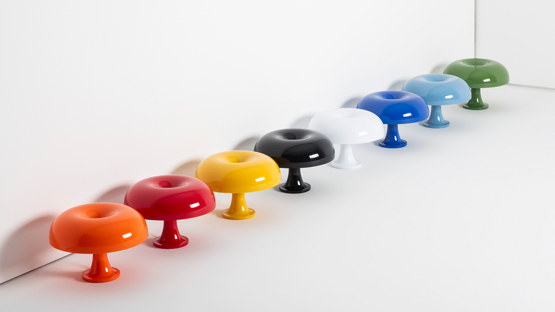 Otto lampade da tavolo Nessino di Artemide a forma di ciambella lucida in vari colori: giallo, arancione, rosso, bianco, nero, blu, azzurro e verde