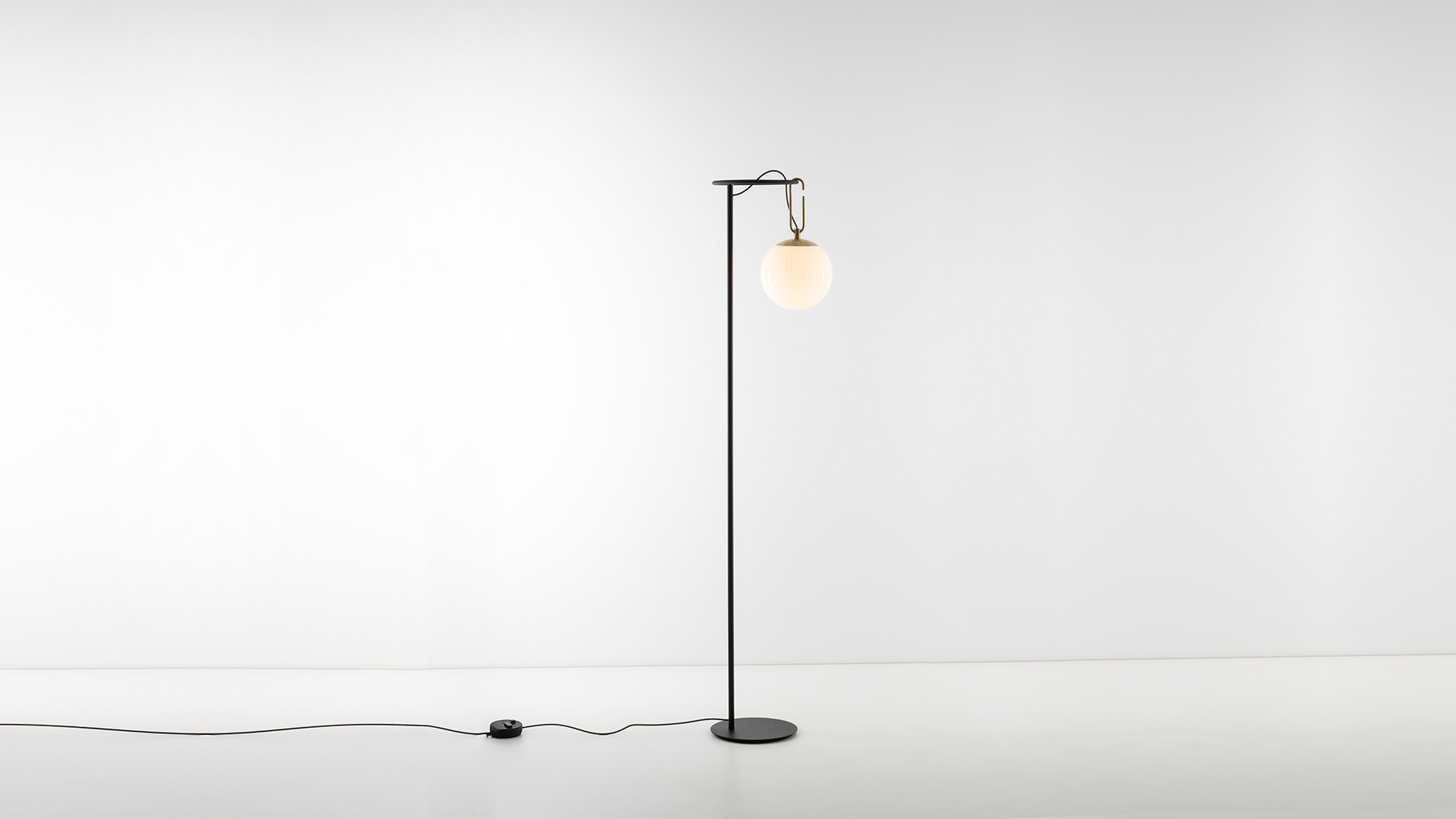 Lampada da terra Artemide NH Terra: alto fusto in metallo nero con base circolare, diffusore a globo in vetro opalino sospeso da un gancio in ottone