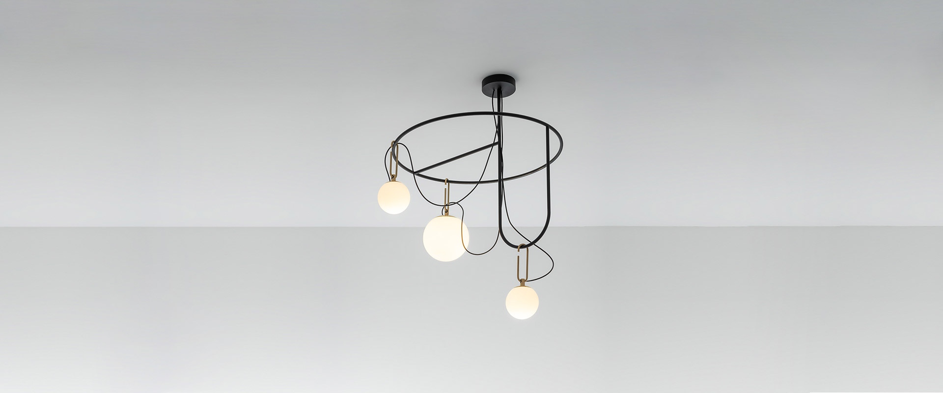 Artemide NH suspension lamp: two opal glass spheres hanging from brass horizontal bars on black cables, against blue background
