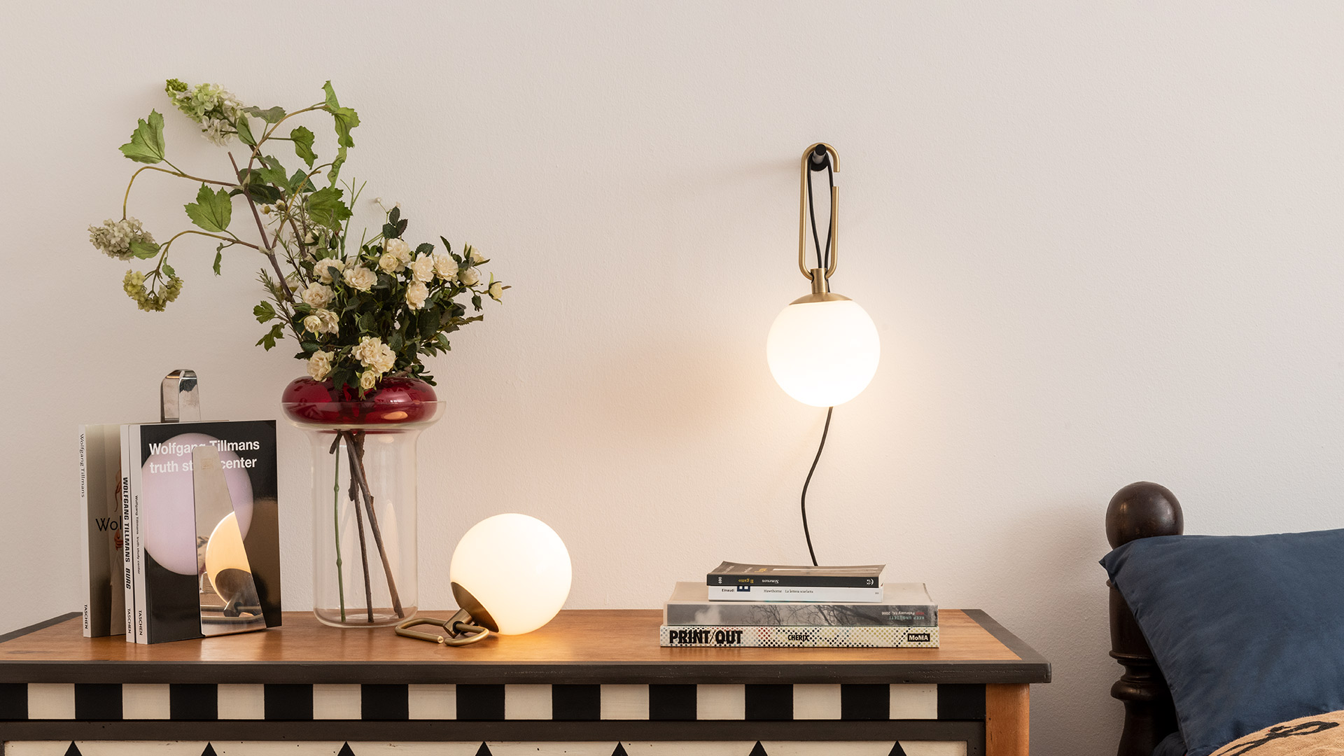 Artemide nh Parete wall lamp with brass frame and opal glass globe, mounted above a bedside table in an elegant bedroom