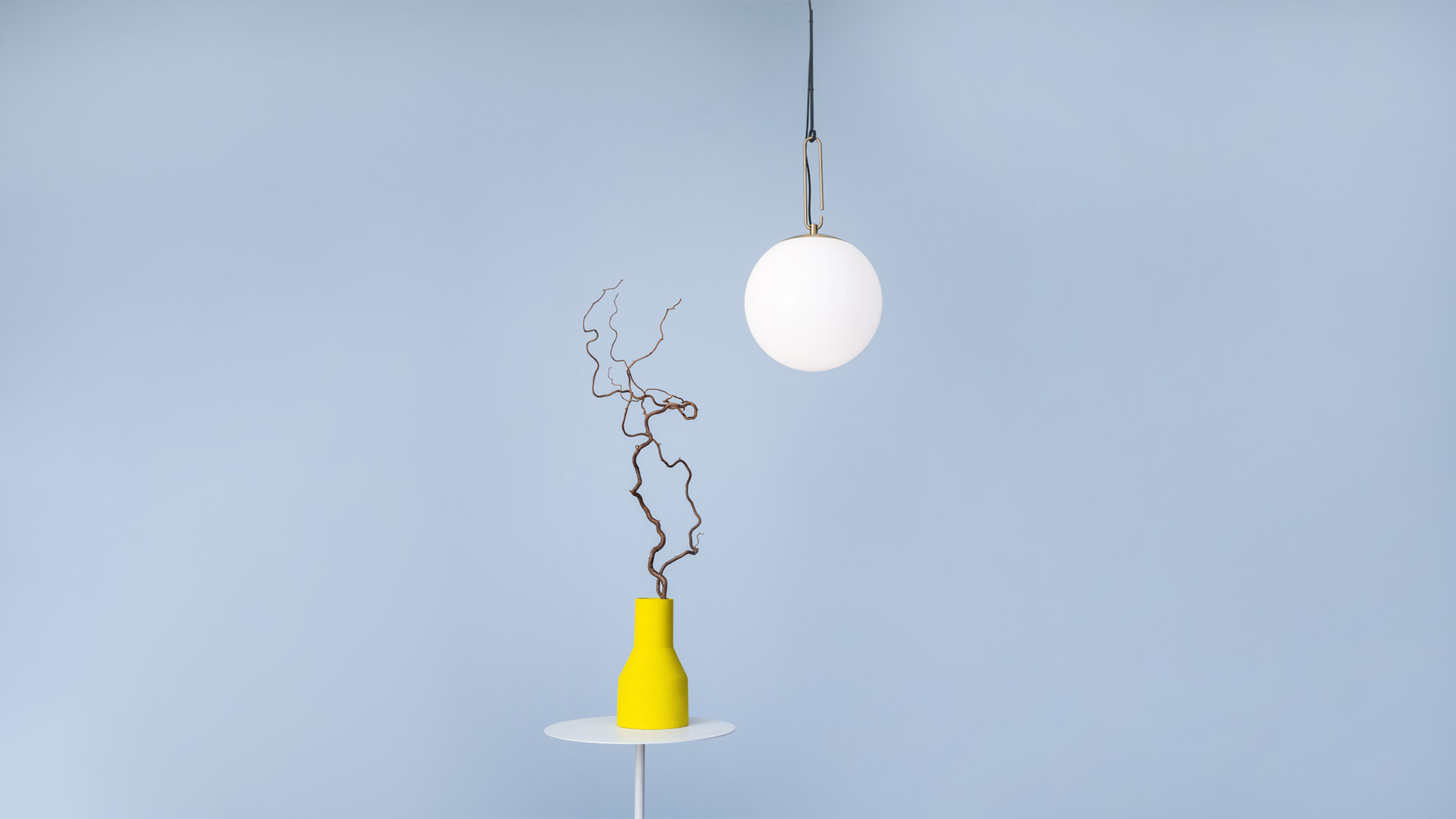 Artemide NH pendant lamp with opal white glass sphere suspended over a yellow vase with decorative branches on a white side table