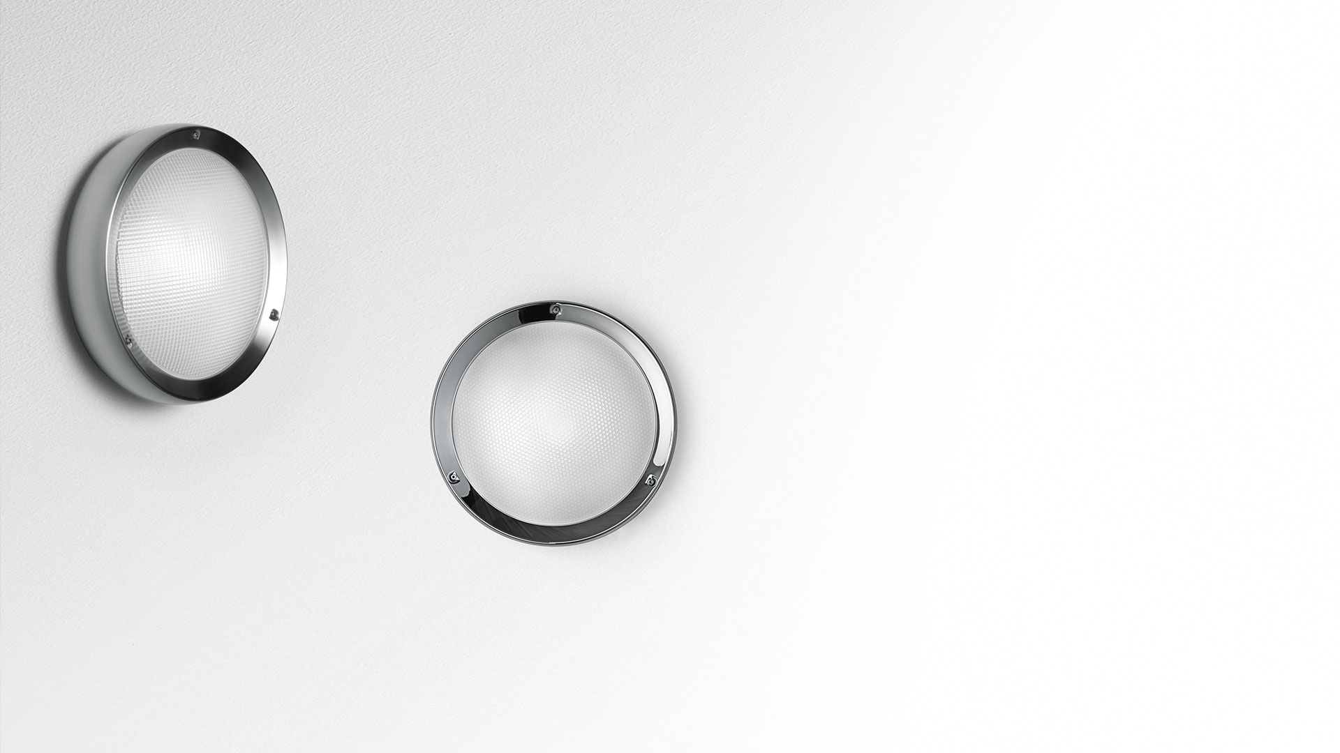 Due applique da parete Artemide Niki con cornici circolari cromate e diffusori in vetro satinato, montate su parete bianca