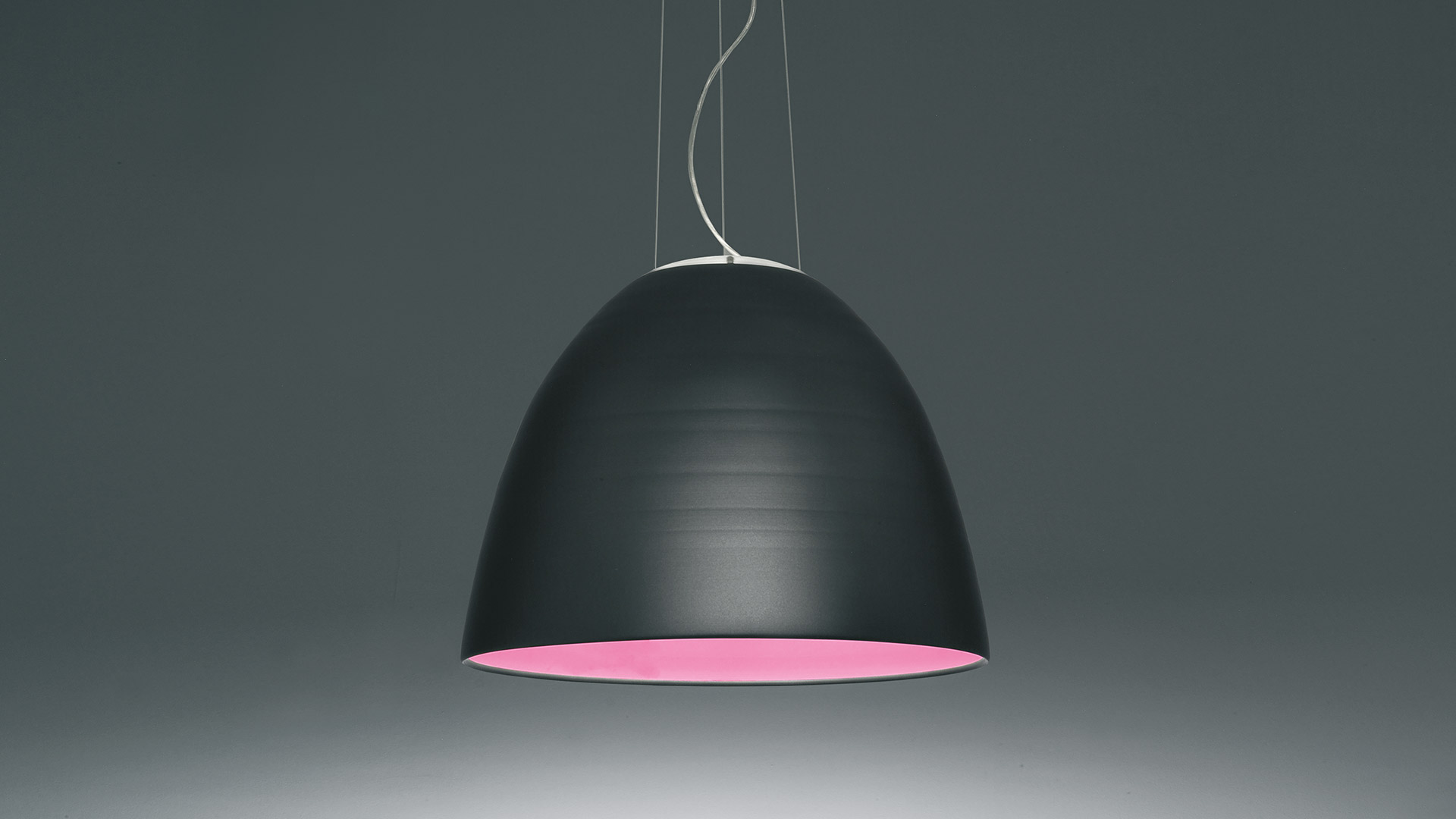 Tre lampade a sospensione Artemide Nur in nero opaco con interno dorato caldo, appese a diverse altezze su sottili cavi