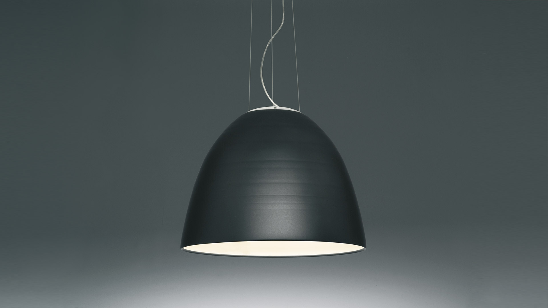 Arena equestre coperta con lampade a sospensione Artemide Nur 1618 su soffitto bianco inclinato, che illuminano il piano sabbioso con cavallo e cavalieri