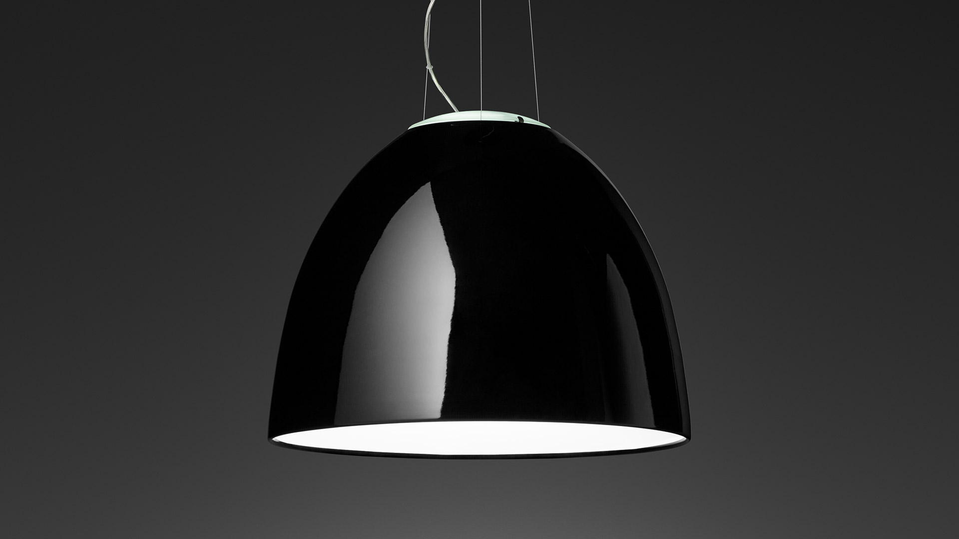 Sala pausa ufficio moderna con tre lampade a sospensione Artemide Nur Gloss nere sopra un'area pranzo con sedute a panca rosse e tavoli bianchi.