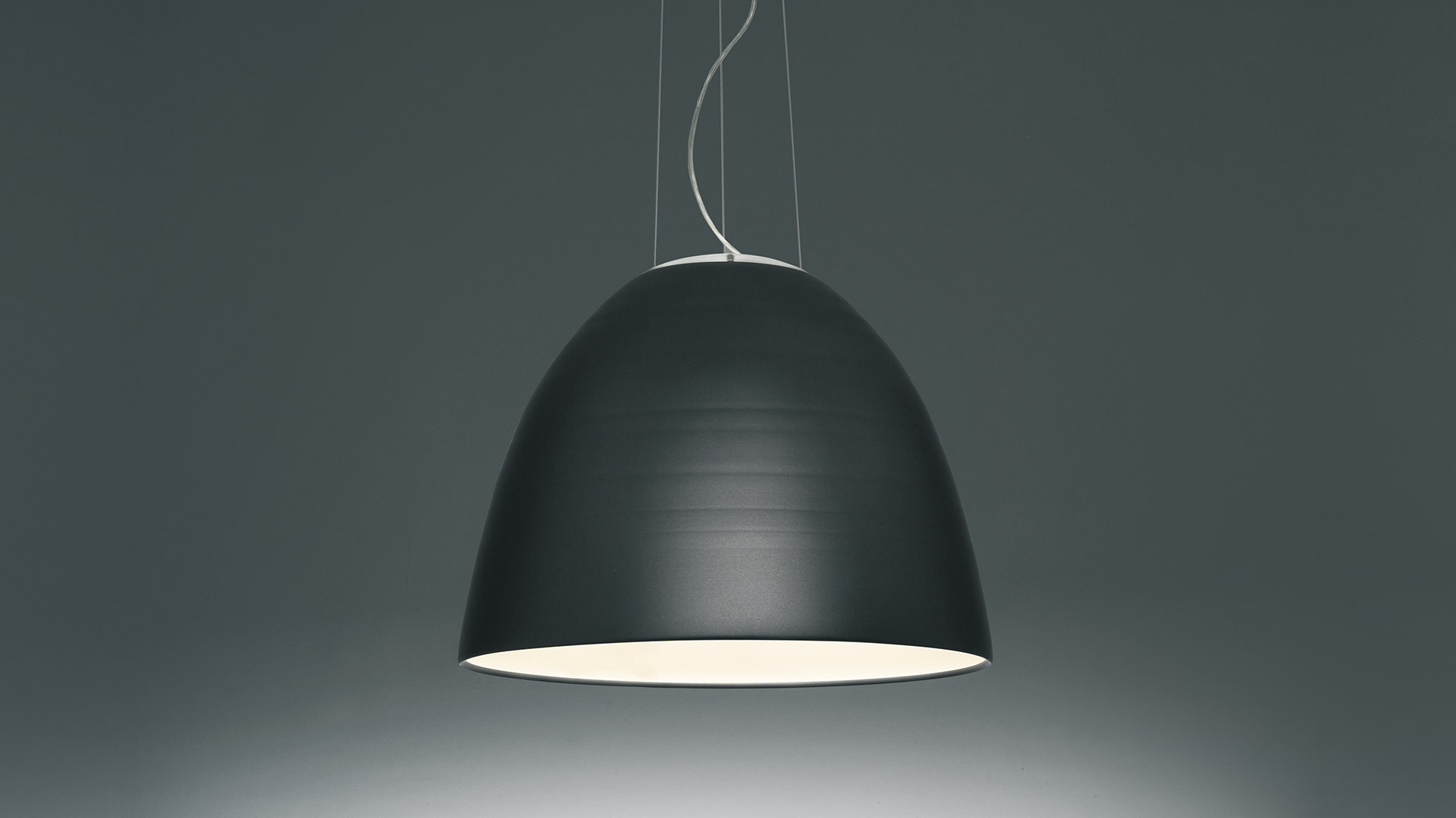 Fila di lampade a sospensione Artemide Nur con esterno scuro e interno rosa vibrante che illuminano un lungo tavolo in legno in un bar moderno