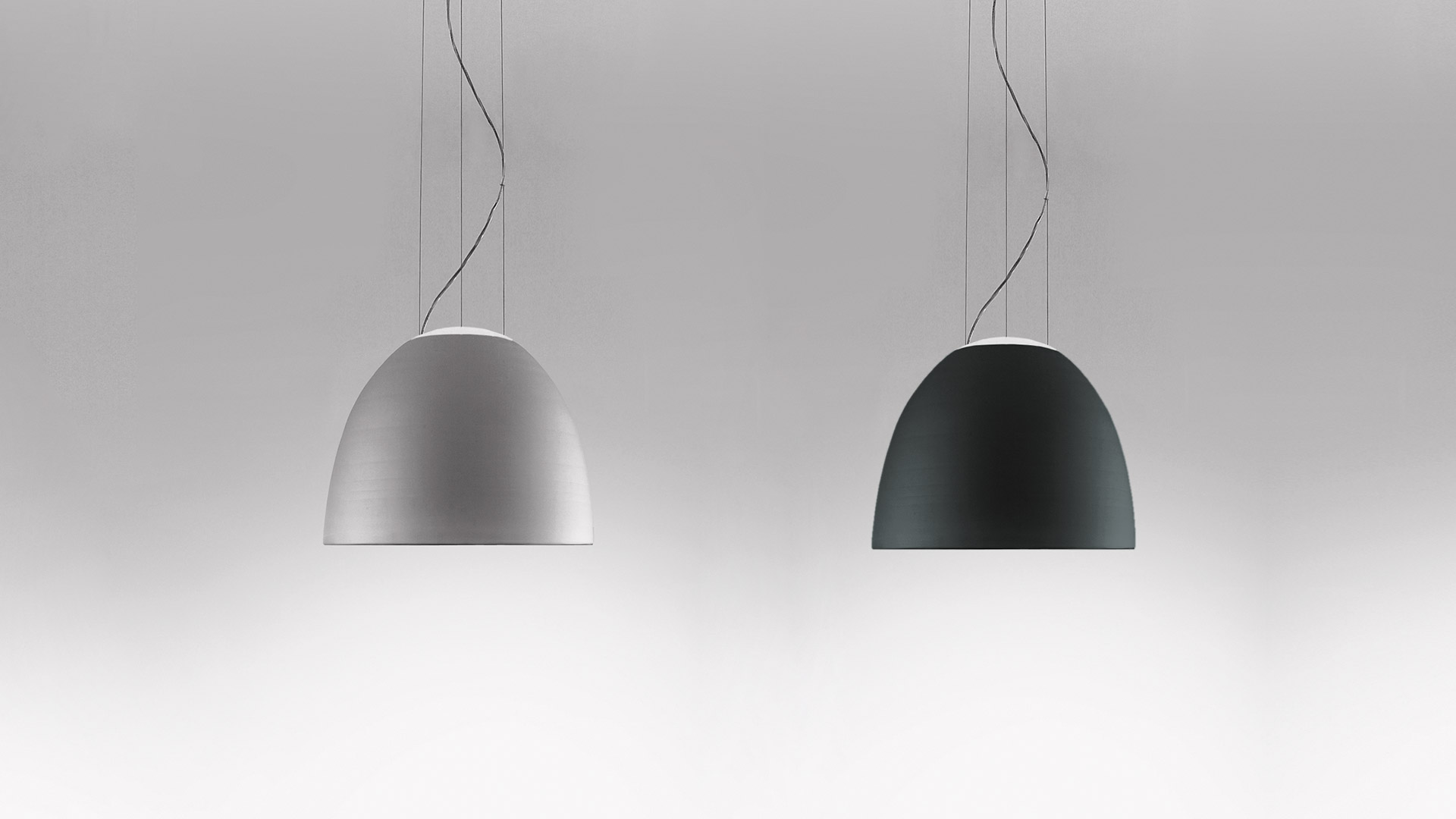 Two Artemide Nur Mini ceiling lights: left in light grey, right in dark grey, both with dome-shaped shades emitting warm diffused light