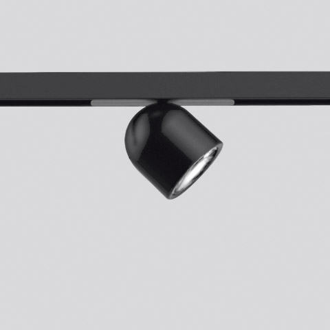 Artemide Olmo Spot: faretto da binario nero compatto con testa arrotondata, montato su sistema a binario nero, inclinato.
