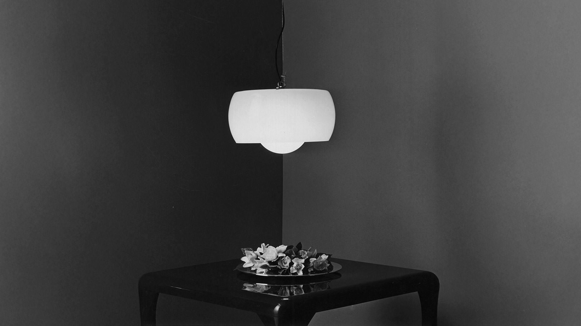 Artemide Omega pendant lamp with rounded white diffuser shade suspended from ceiling by black cord and brushed metal canopy