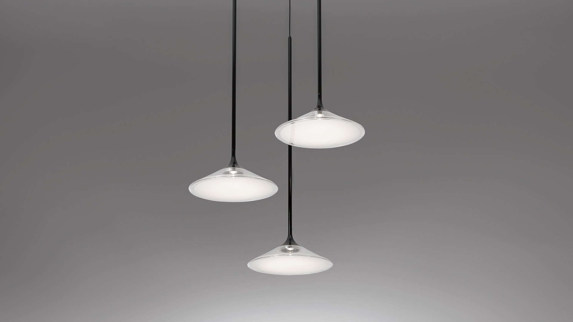 Artemide Orsa Cluster: three pendant lights with flat opal white diffusers and chrome details, suspended at varying heights on black cords