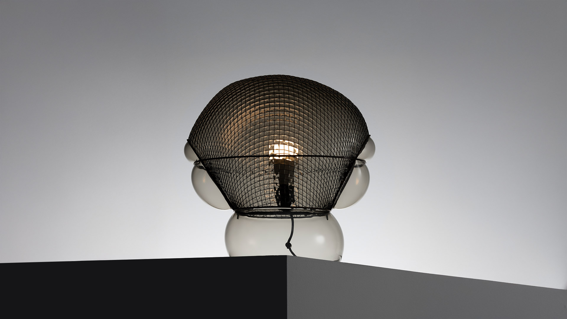 Dettaglio lampada Artemide Patroclo: paralume in rete metallica intrecciata con motivo a rombi che avvolge un diffusore sferico in cromo lucido