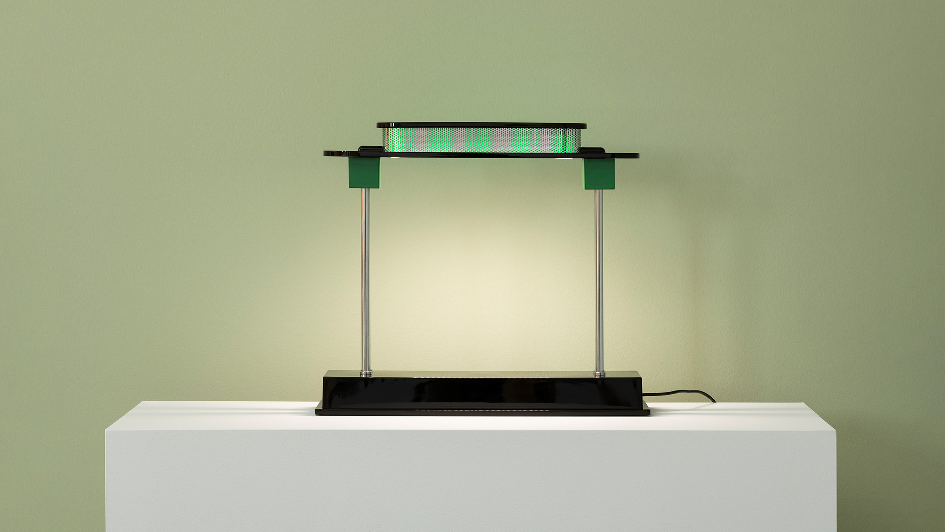 Primo piano della lampada Artemide Pausania: paralume in metallo forato scuro che emette vivace luce LED verde attraverso fori circolari
