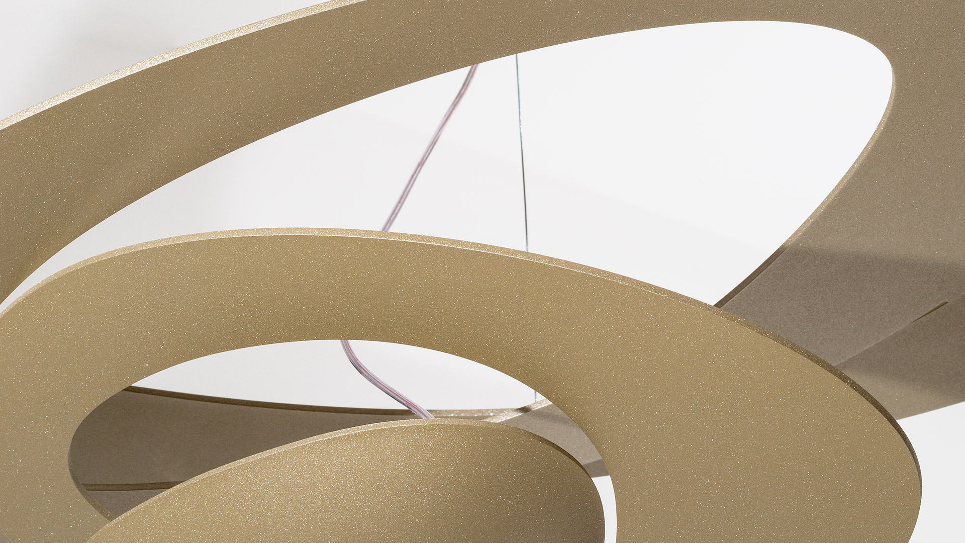 Lampada a sospensione Artemide Pirce Sospensione con anelli a spirale dorati che emettono luce calda, appesa su una parete a pannelli color verde acqua