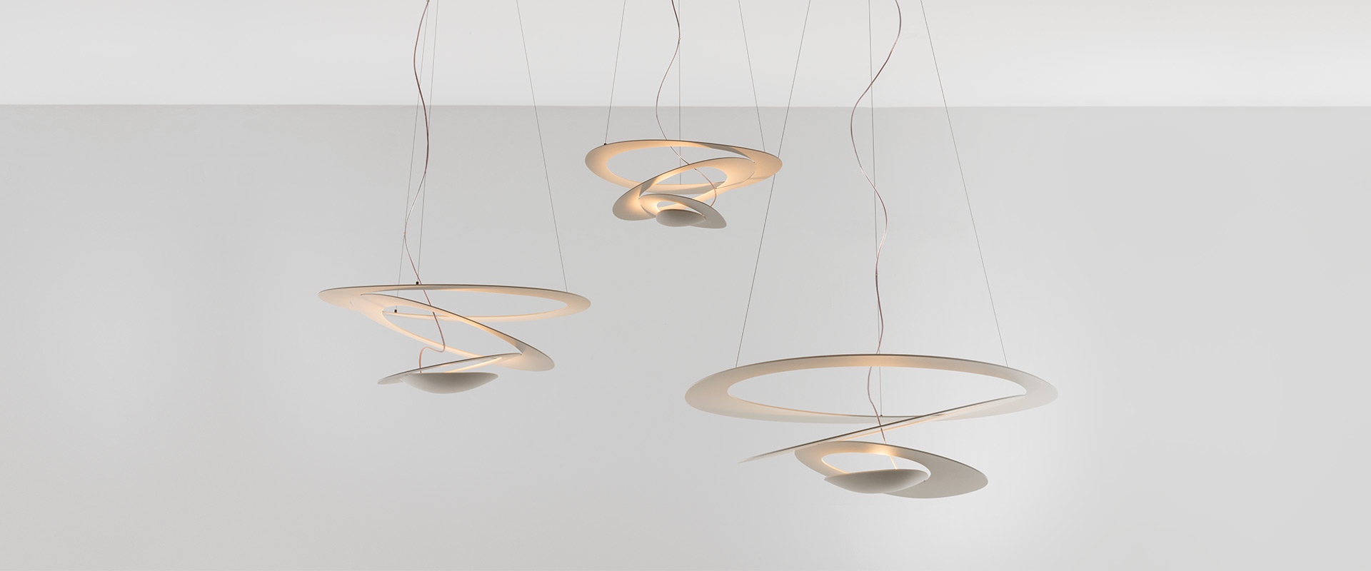 Lampada a sospensione Artemide Pirce: paralume bianco scultoreo a spirale con anelli concentrici che emettono luce diffusa morbida, sospesa da sottili cavi