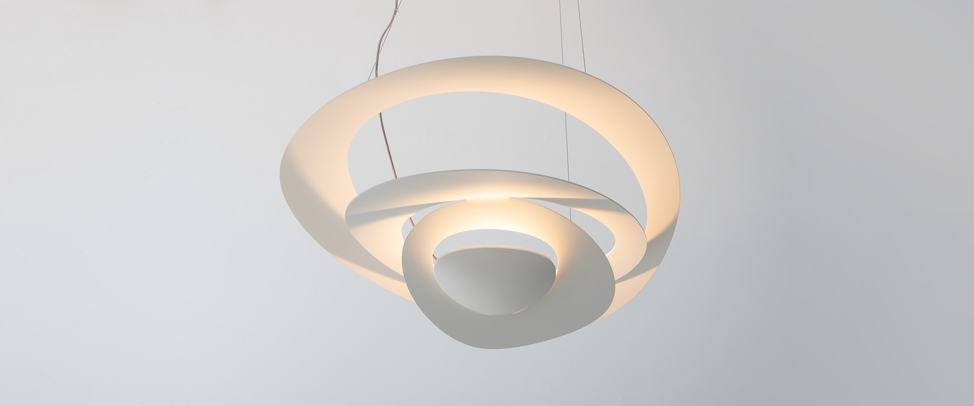 Lampada a sospensione Artemide Pirce: paralumi in alluminio a spirale intrecciata che emettono luce dorata calda, appesi a sottili cavi