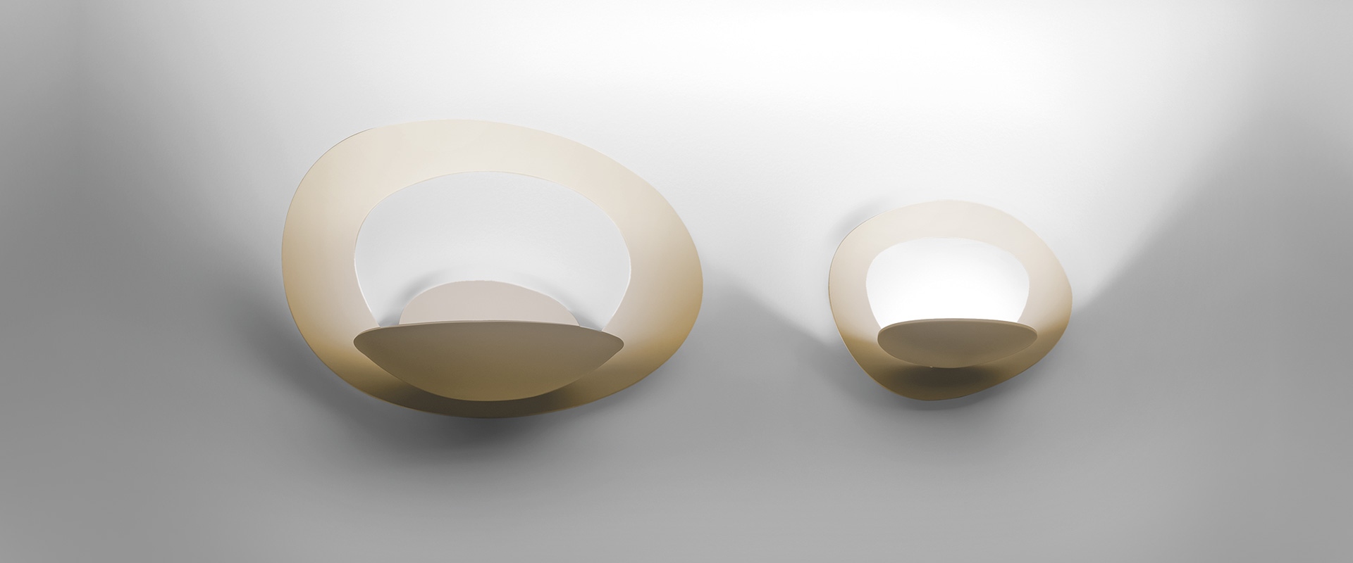 Two Artemide Pirce Parete wall lamps in golden beige: large and small sizes, organic shell shape emitting warm white upward light