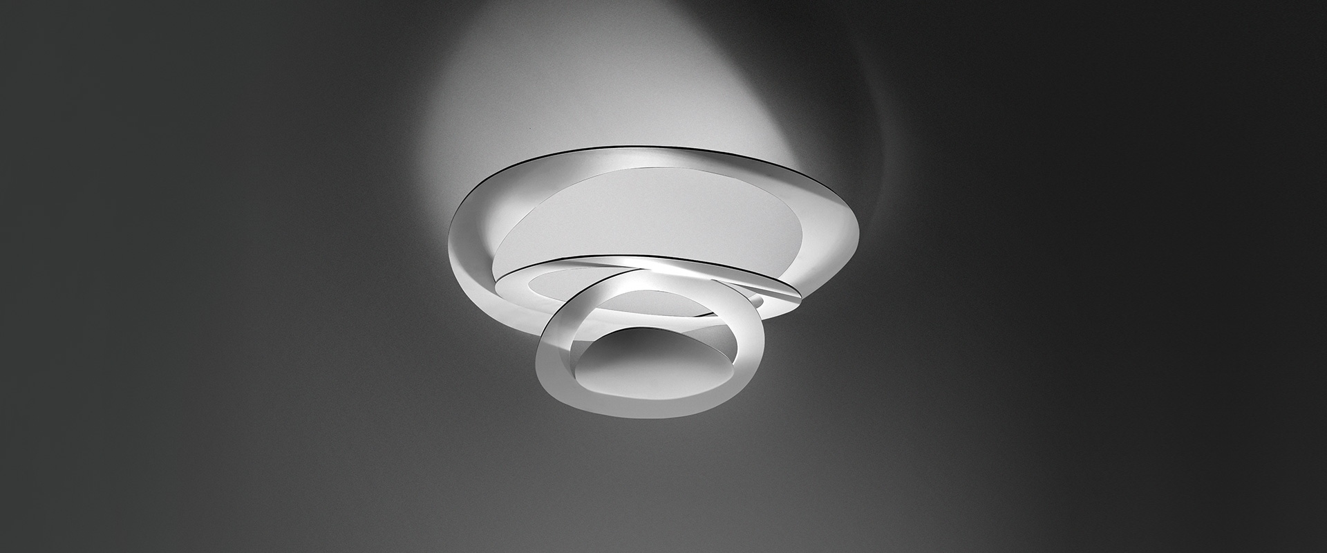 Artemide Pirce Soffitto ceiling lamp with white sculptural spiral diffuser casting elegant curved shadows on grey ceiling