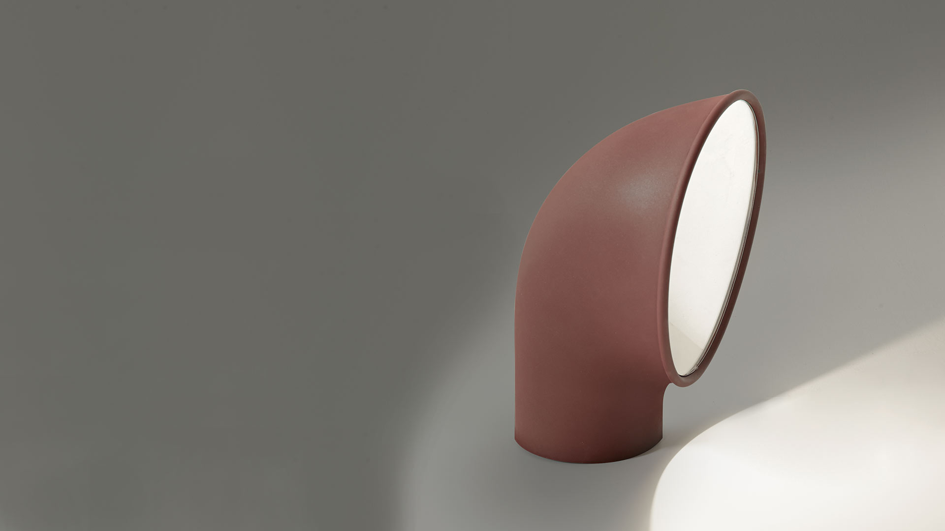 Artemide Piroscafo table lamp: curved terracotta-red tubular body bent at 90°, emitting soft white light from its circular opening