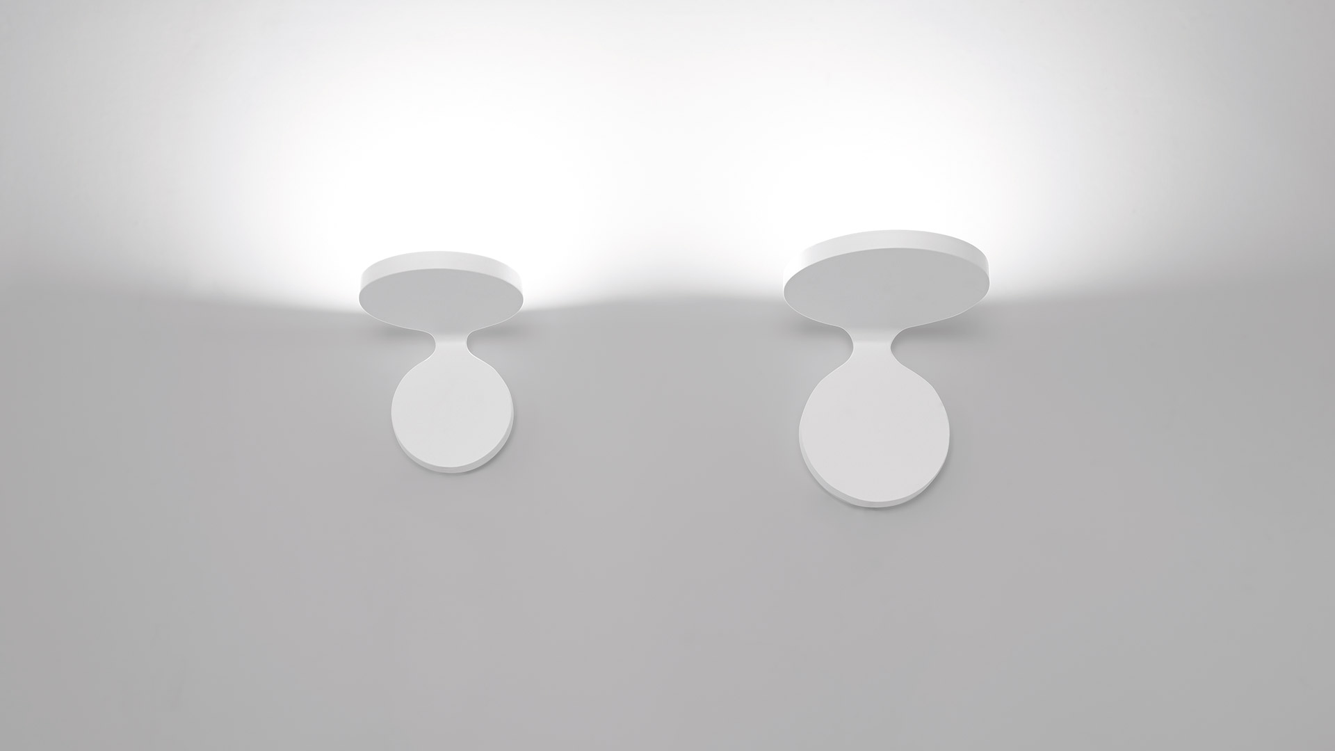 Due faretti da parete/soffitto Artemide Rea in bianco, con teste circolari inclinate verso il basso che proiettano luce diffusa verso l'alto
