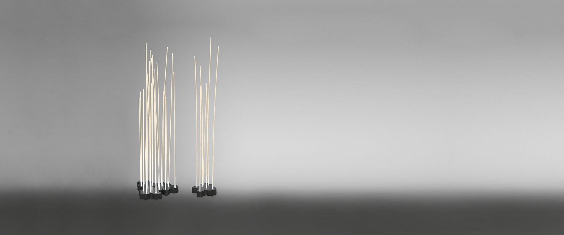 Lampade Artemide Reeds Outdoor disposte tra piante da giardino al crepuscolo, che imitano steli di bambù illuminati accanto a fiori selvatici viola