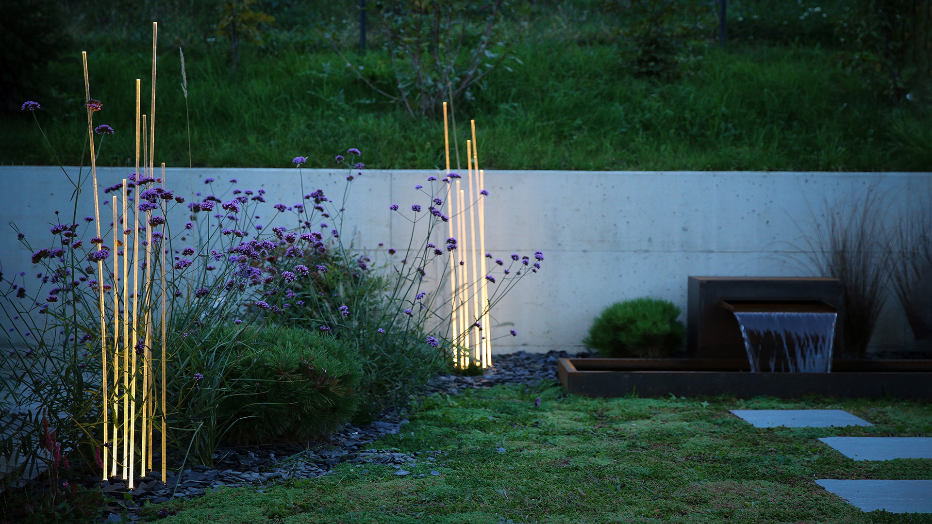 Lampade da terra Artemide Reeds Outdoor: due gruppi di sottili steli verticali luminosi su basi scure, che evocano canne naturali