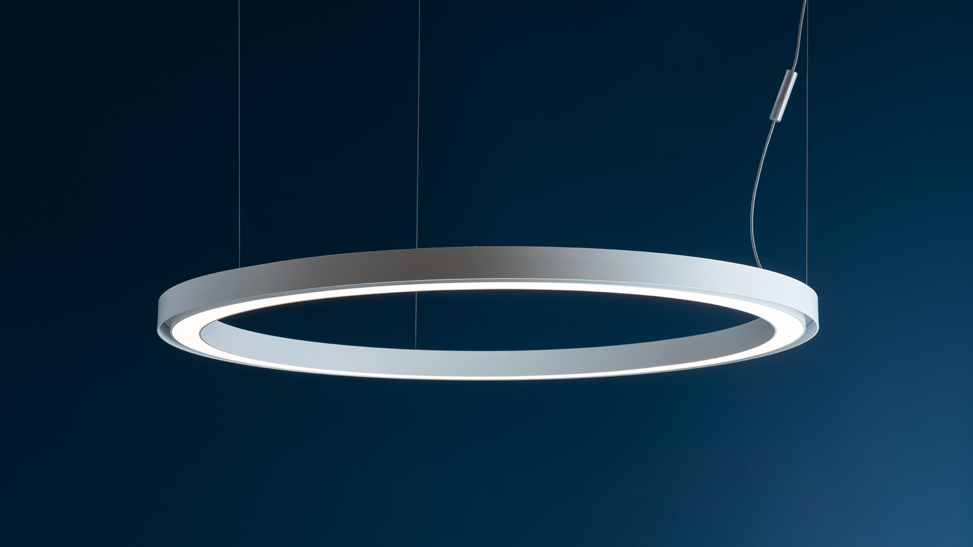 Lampade a sospensione Artemide Ripple: quattro anelli LED circolari grigi di diverse dimensioni, sospesi sopra un tavolo scuro con un piccolo vaso